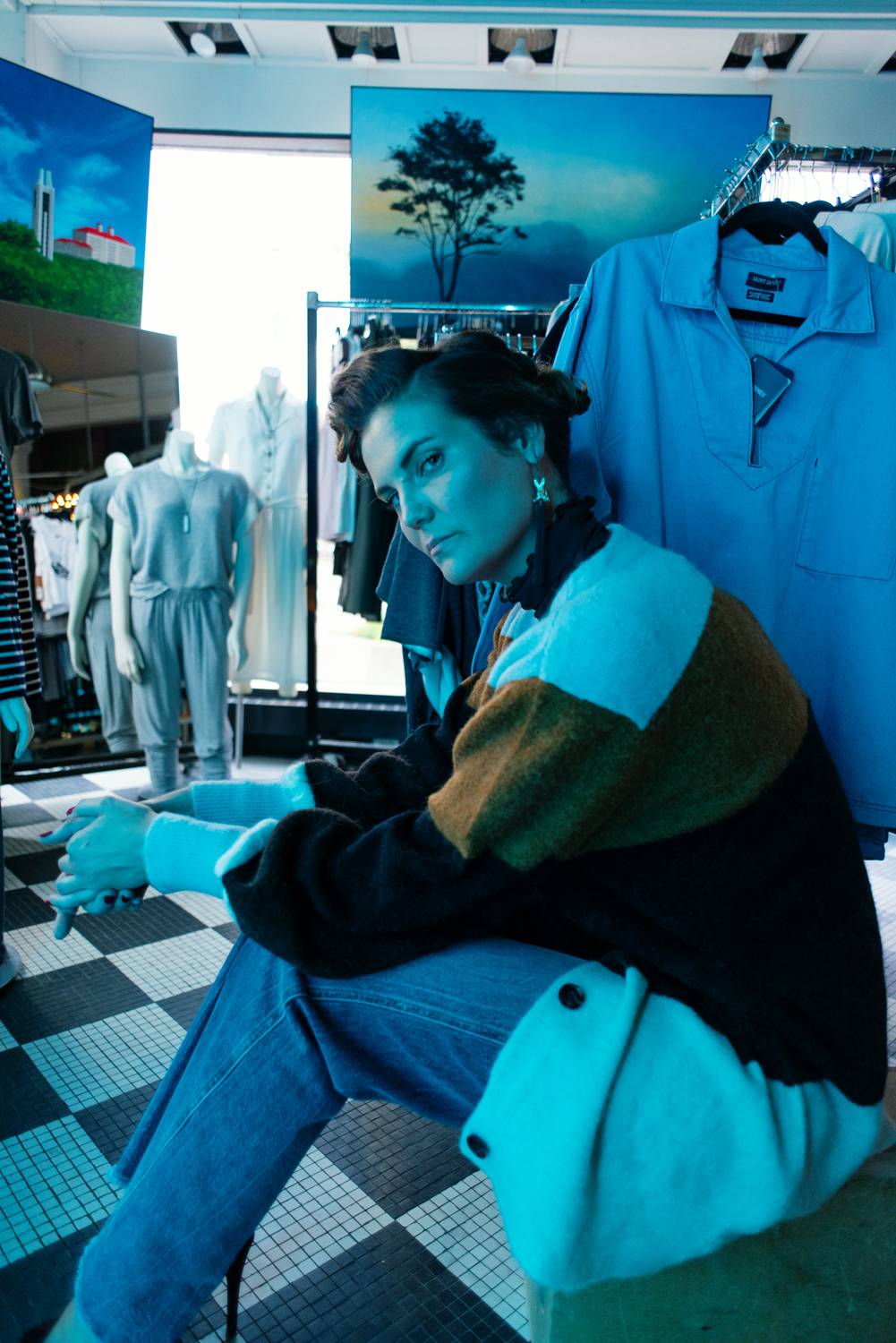 woman sitting down in a department store surrounded by racks of clothing 